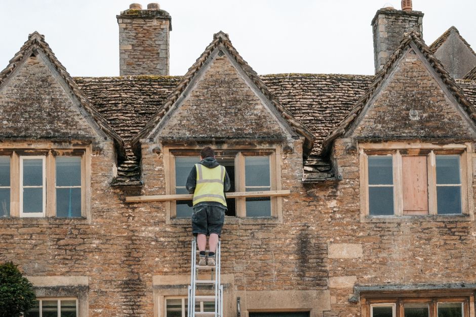 Inside a professional house removal setting, a team from Removals Paddington is loading a large, rectangular cardboard box wrapped in clear plastic onto a moving trolley. The scene shows a spacious ro