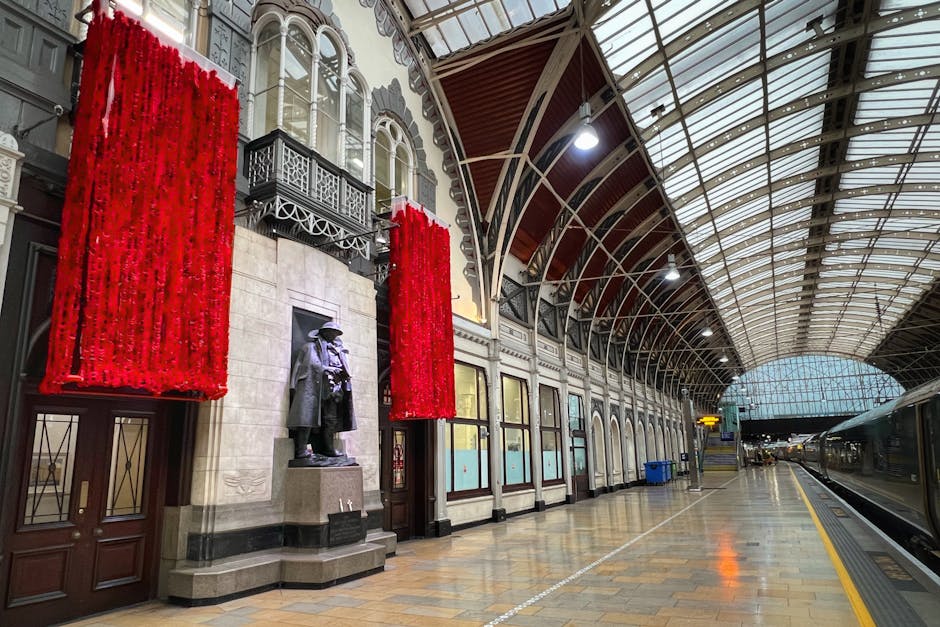 Photograph of Paddington Station's arched glass and metal entrance canopy, showcasing decorative metalwork and the station's sign. The sky is partly cloudy with blue patches and white clouds visible t